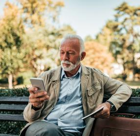 Senior man on sunny park bench using smartphone