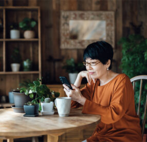 Senior Asian woman sitting at table, shopping for hearing aids on her smartphone